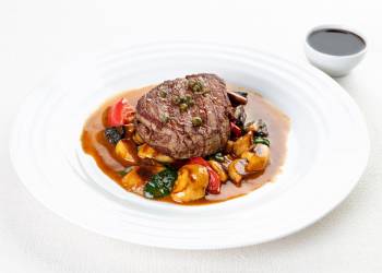 Filet mignon with a side dish of porcini mushrooms, tomatoes, capers and pepper sauce